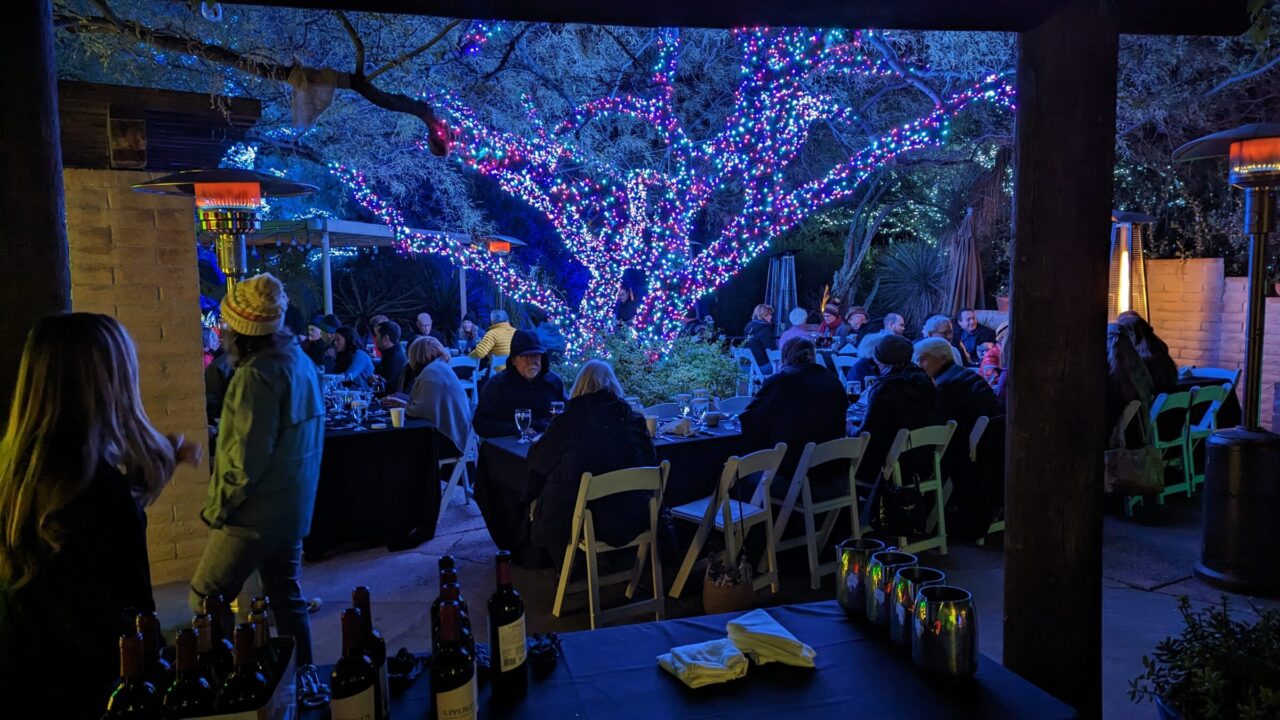 Photograph of people seated at tables around a tree decorated with lights